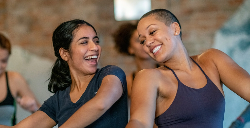 Two women laughing together mid-movement in an exercise class